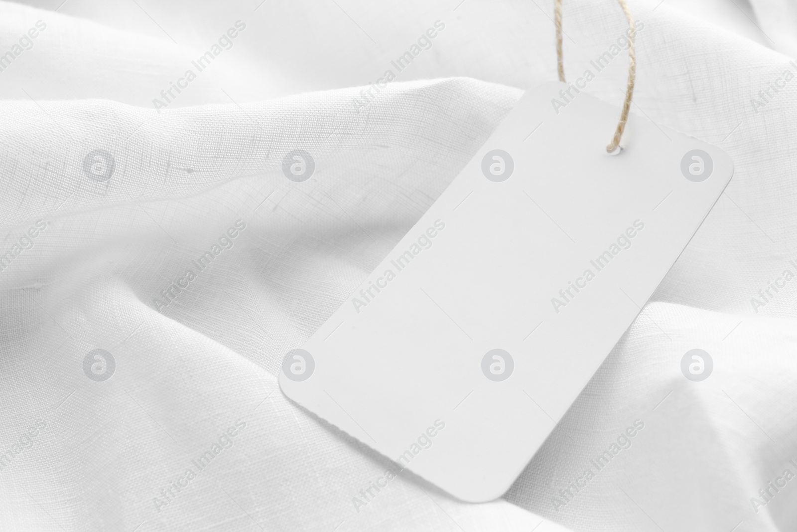 Photo of Cardboard tag with space for text on white fabric, closeup