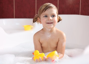 Photo of Smiling girl bathing with toy ducks in tub