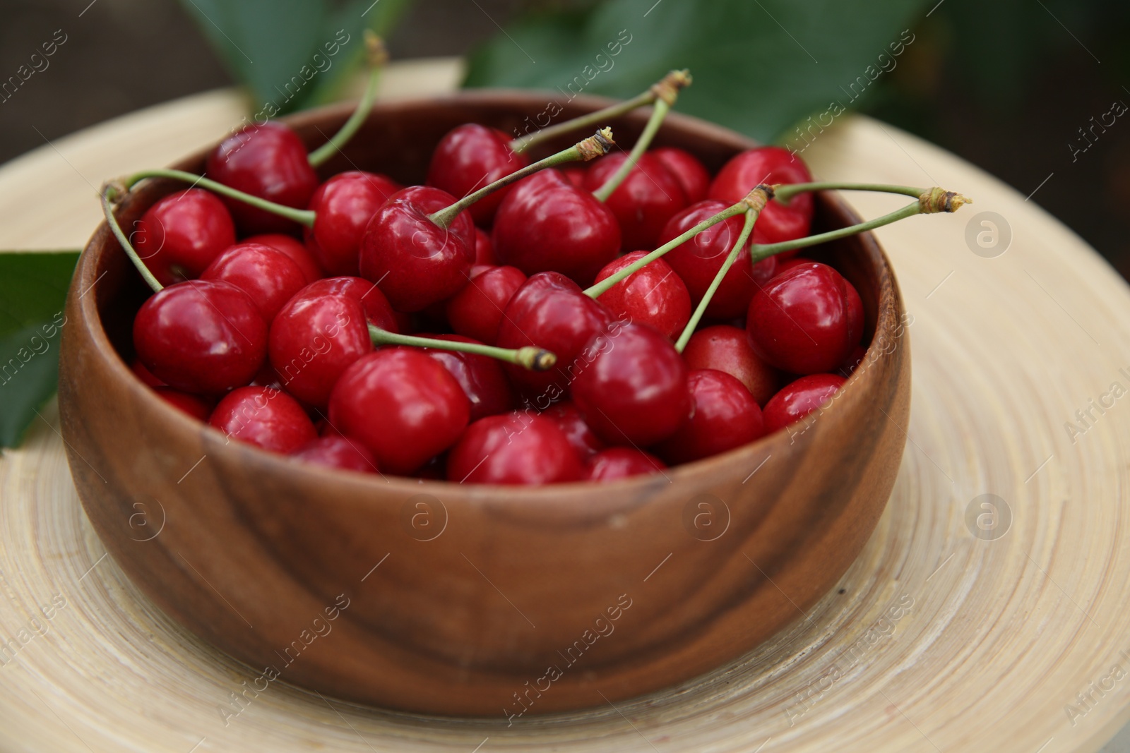 Photo of Tasty ripe red cherries in wooden bowl outdoors