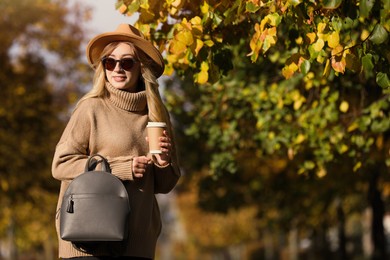 Photo of Young woman with stylish backpack and hot drink on autumn day