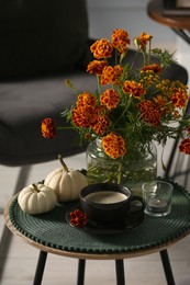 Photo of Beautiful autumn flowers, cup of coffee and pumpkins on side table indoors