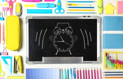 Small blackboard with drawn alarm clock and different stationery on white wooden table, flat lay . Time to school