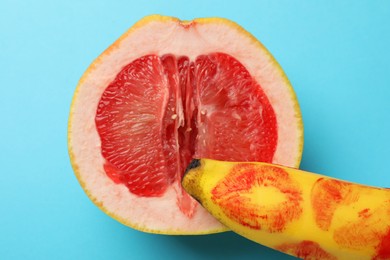 Photo of Banana with red lipstick marks and half of grapefruit on light blue background, top view. Sex concept