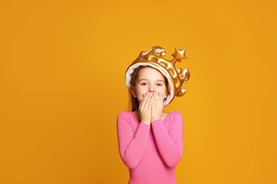 Cute girl in inflatable crown on yellow background. Little princess