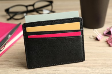 Leather business card holder with colorful cards on wooden table, closeup