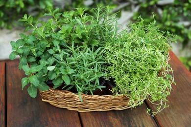 Photo of Wicker basket with fresh mint, thyme and rosemary on wooden table outdoors. Aromatic herbs