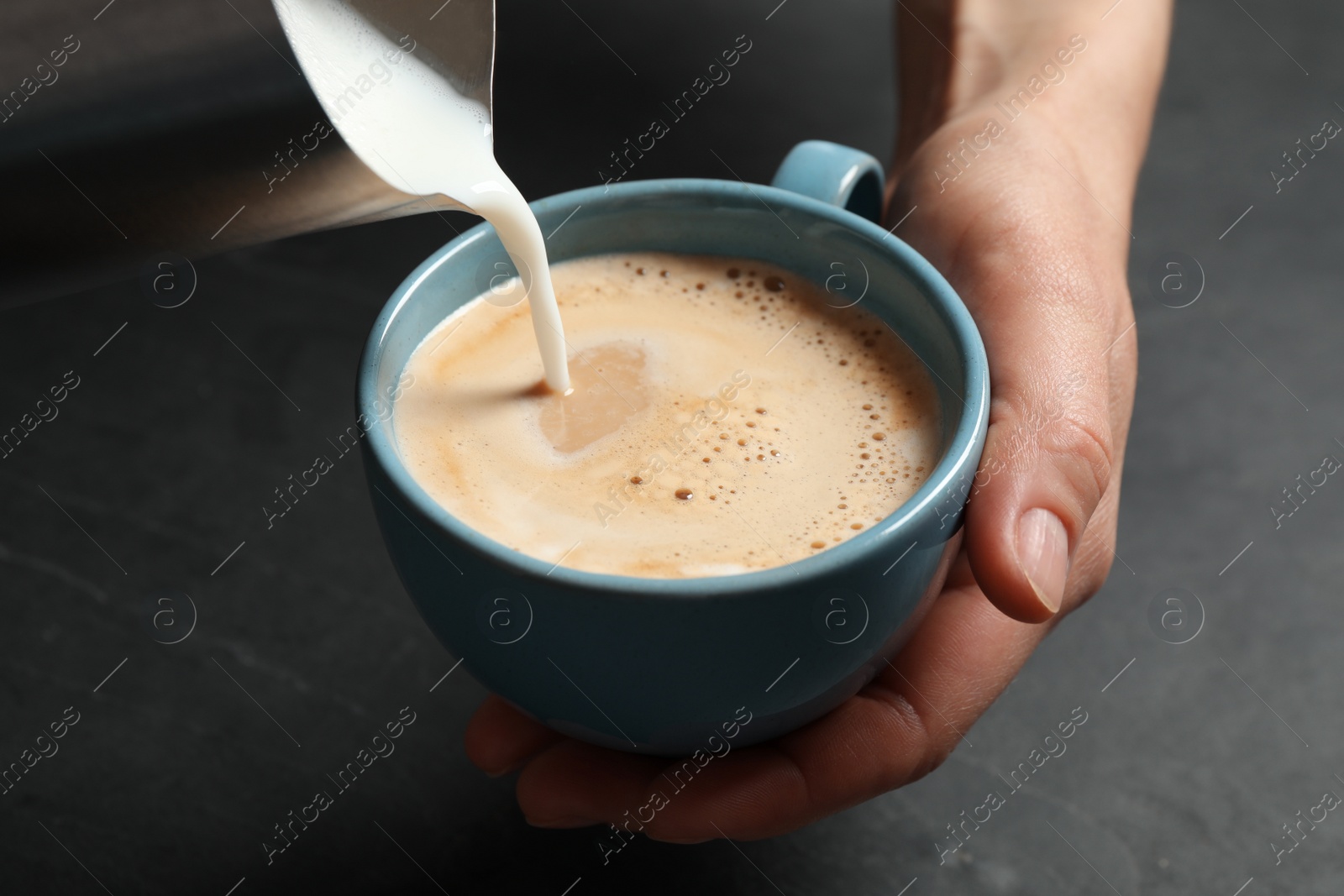 Photo of Woman pouring milk into cup of coffee at black table, closeup