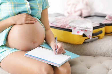 Pregnant woman writing packing list for maternity hospital at home, closeup