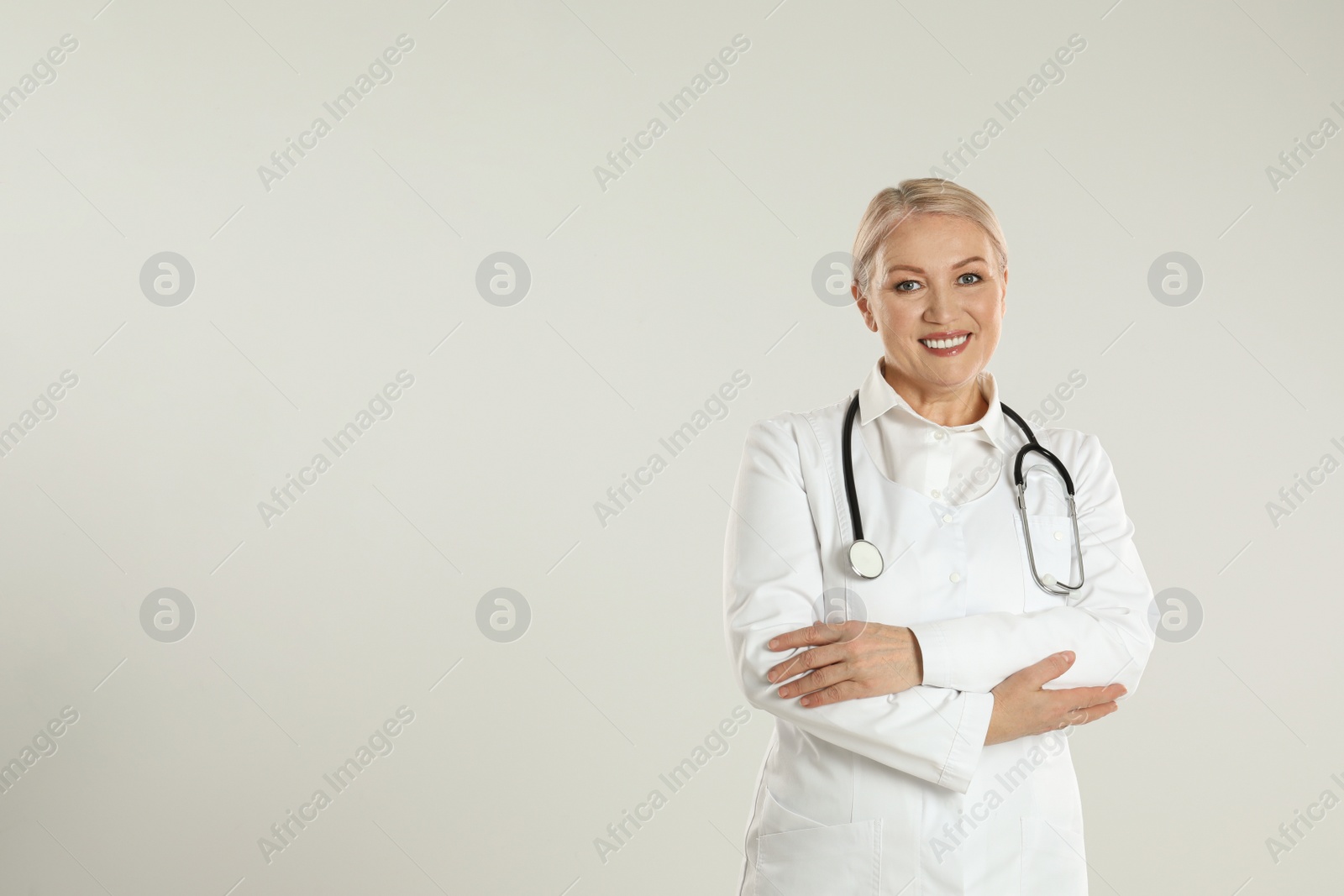 Photo of Portrait of mature doctor with stethoscope on light grey background. Space for text