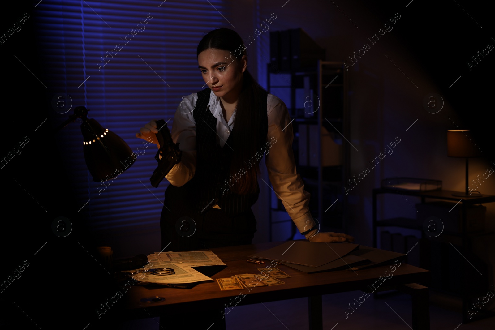 Photo of Professional detective in protective gloves examining handgun indoors at night