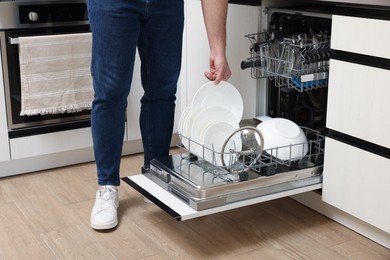 Photo of Man loading dishwasher with plates indoors, closeup