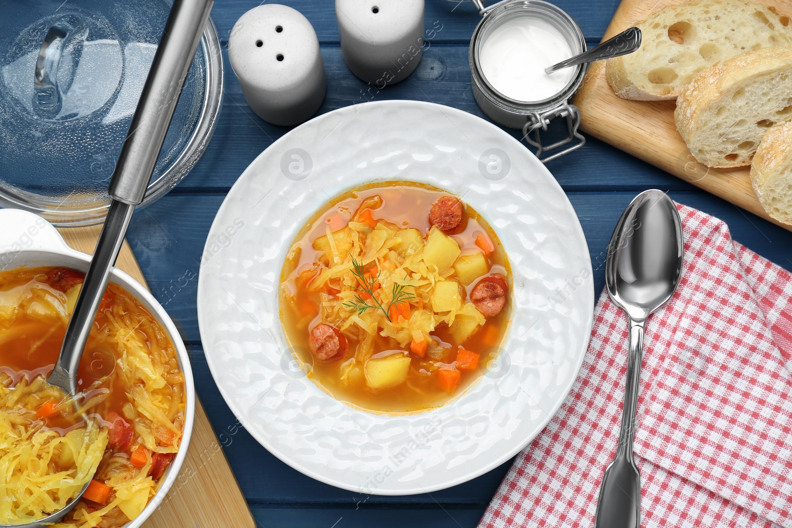 Photo of Delicious sauerkraut soup with smoked sausages served on blue wooden table, flat lay