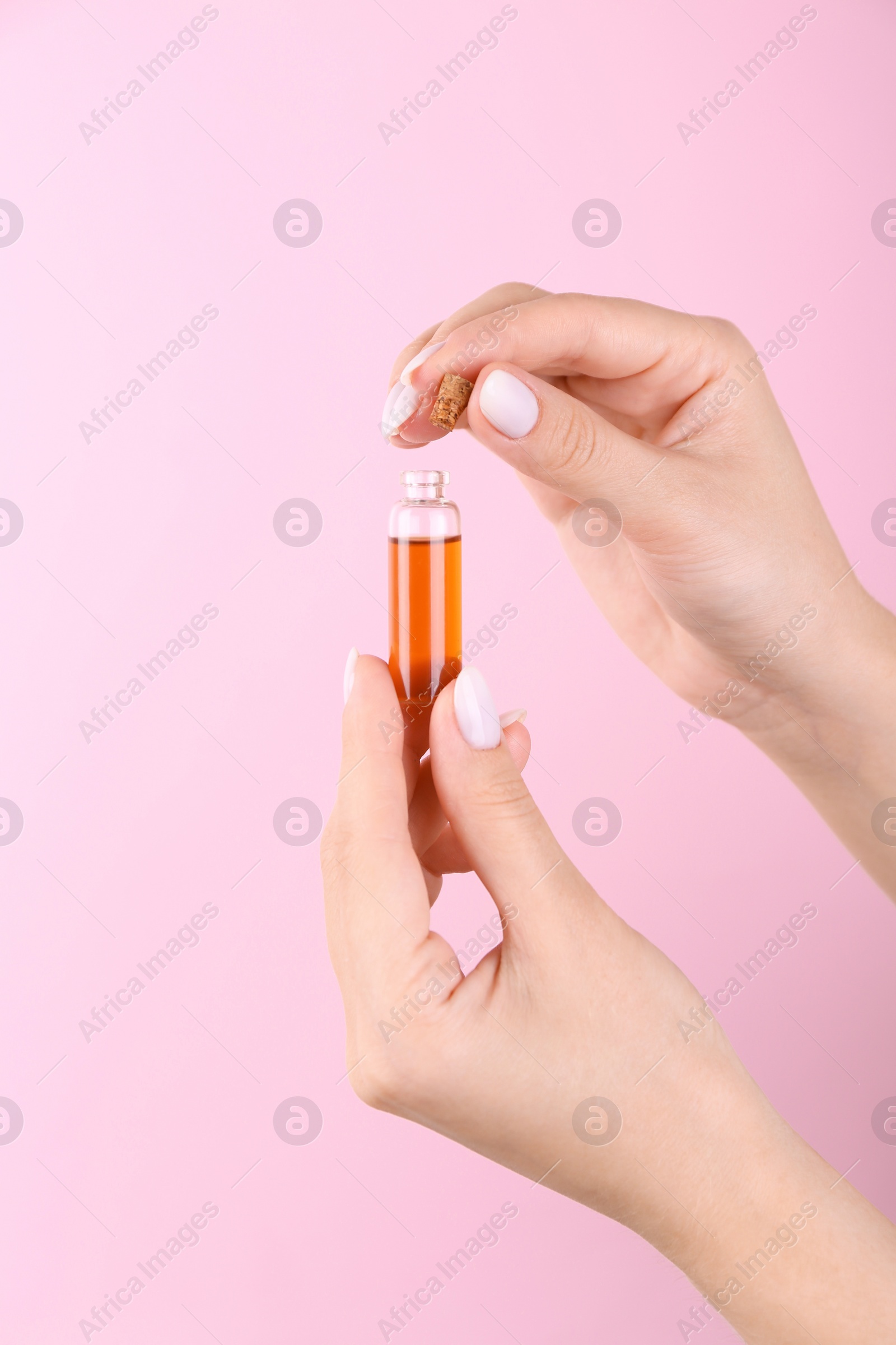 Photo of Woman holding bottle of essential oil on pink background, closeup