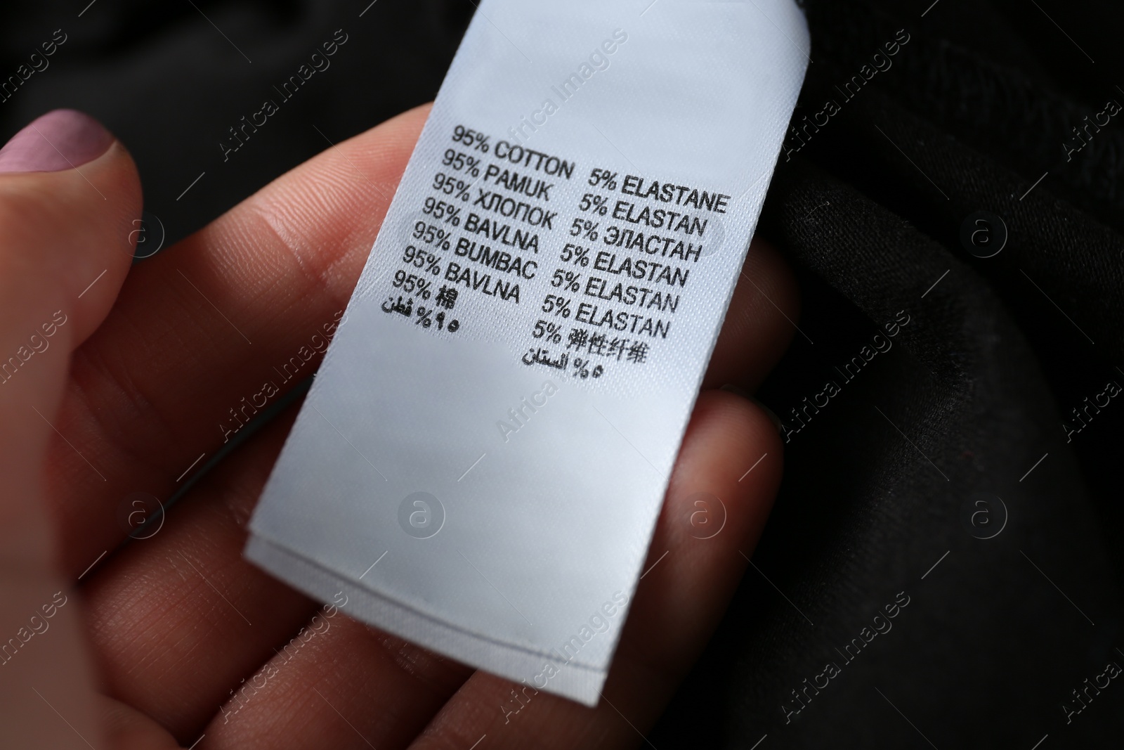 Photo of Woman reading clothing label with material content  on black shirt, closeup