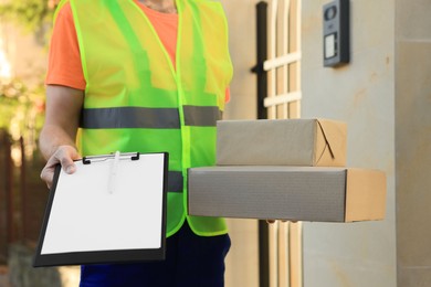 Photo of Courier in uniform holding order receipt and parcels outdoors closeup