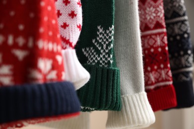 Different Christmas sweaters hanging on rack, closeup