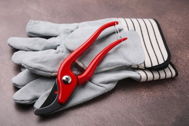 Photo of Pair of gardening gloves and secateurs on brown textured table