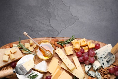Photo of Cheese plate with honey, grapes and nuts on black table, top view. Space for text