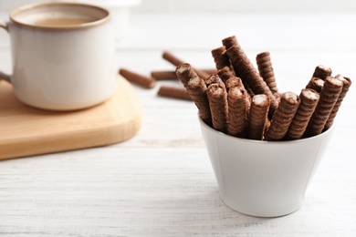 Delicious chocolate wafer rolls in bowl on wooden table. Space for text