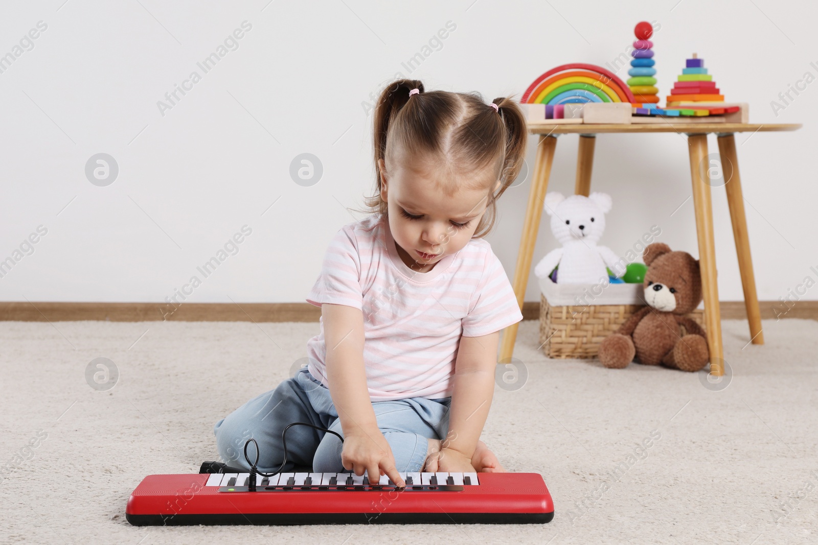Photo of Cute little girl playing with toy piano at home