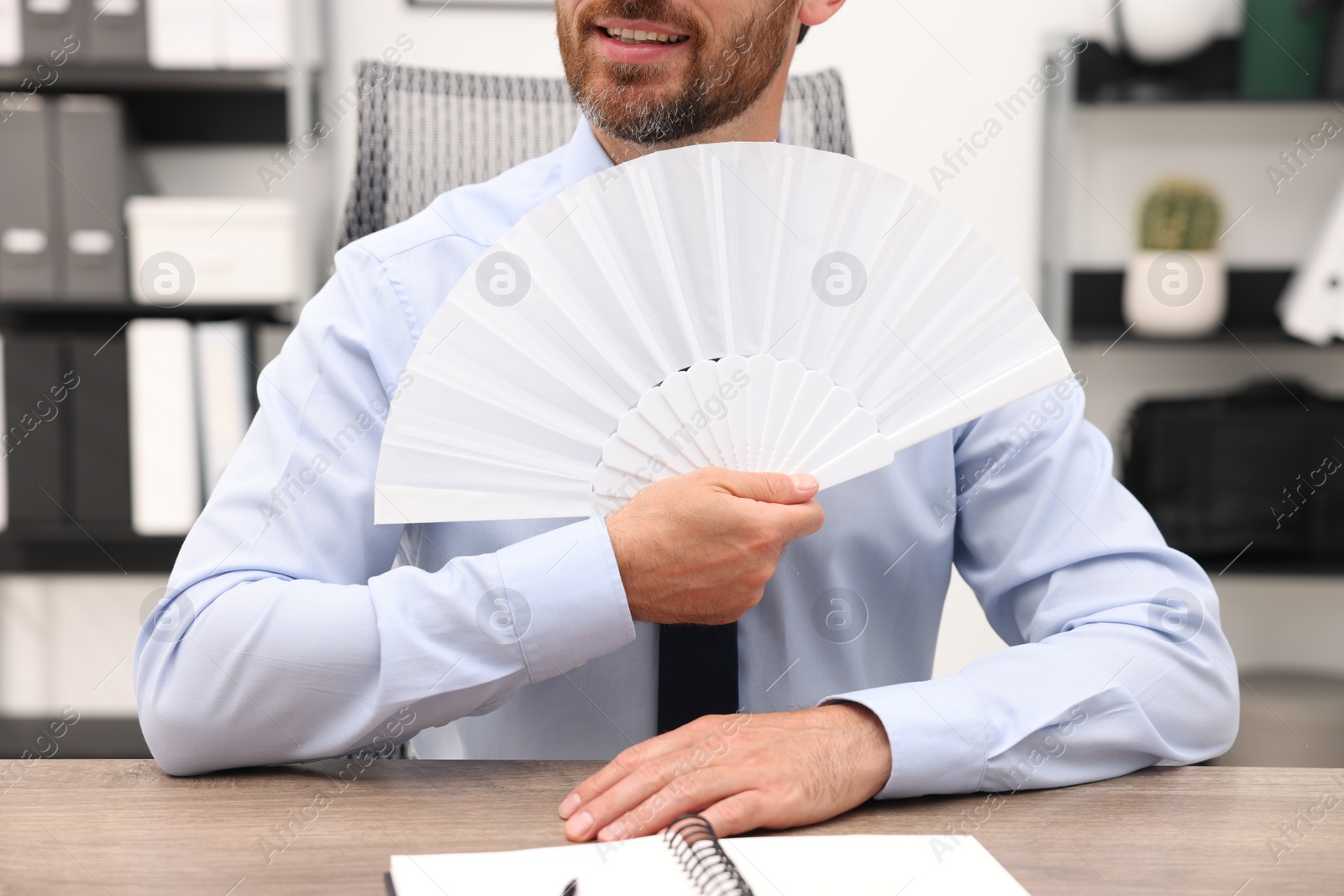 Photo of Businessman with white hand fan at table in office, closeup