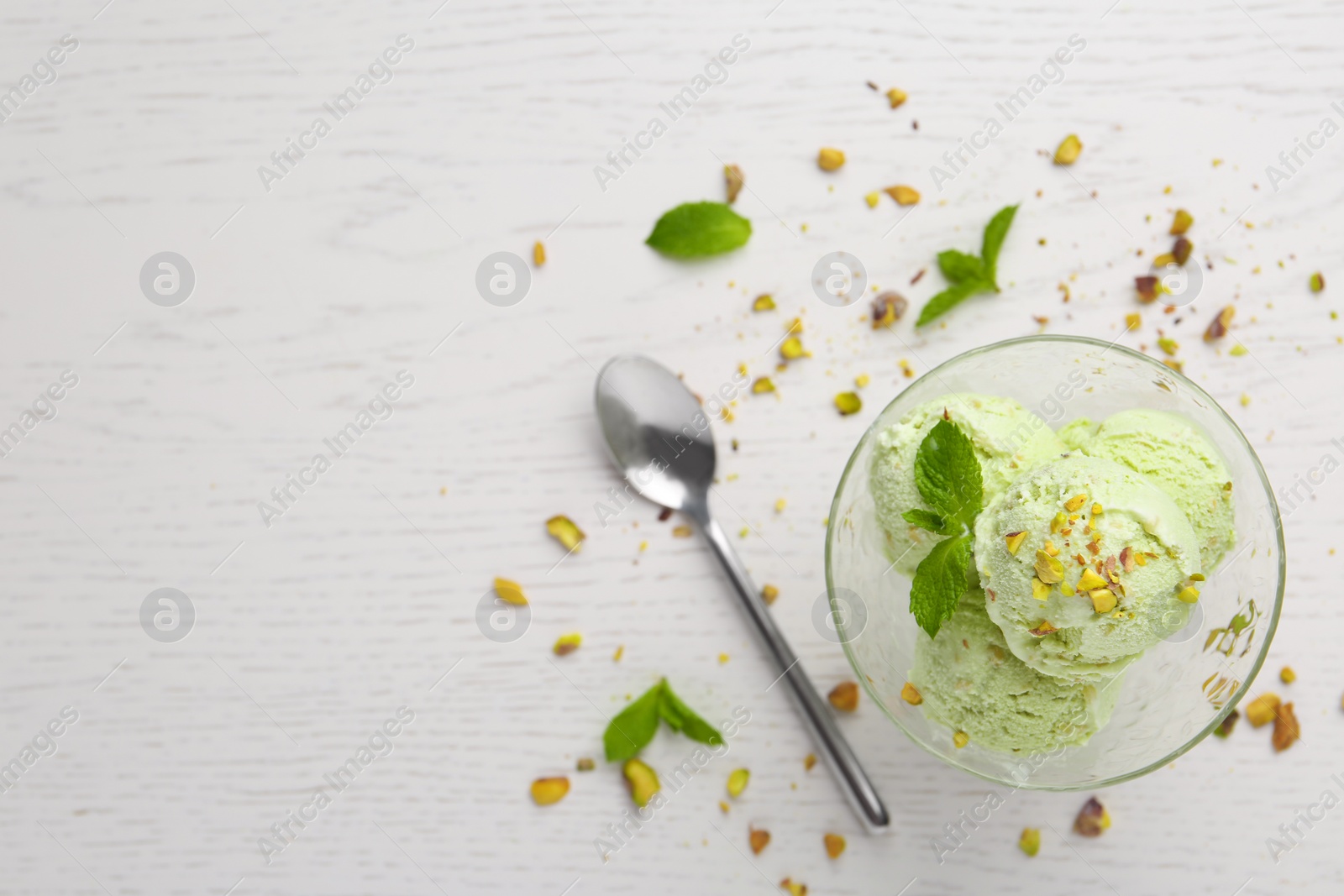 Photo of Delicious green ice cream served in dessert bowl on white wooden table, top view. Space for text