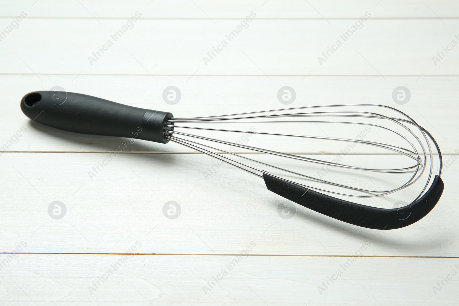 Photo of Metal whisk on white wooden table, closeup