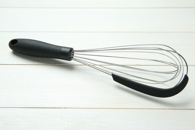 Photo of Metal whisk on white wooden table, closeup