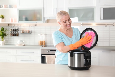 Mature woman cleaning modern multi cooker at table in kitchen