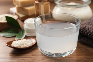 Photo of Homemade natural rice water and cosmetic products on wooden table, closeup