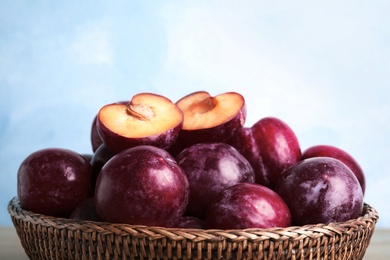 Photo of Delicious ripe plums in wicker bowl against light background, closeup