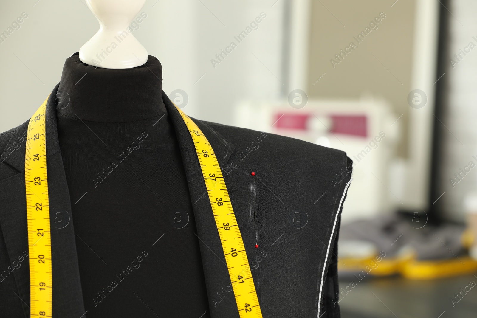 Photo of Mannequin with unfinished jacket and measuring tape in tailor shop, closeup. Space for text