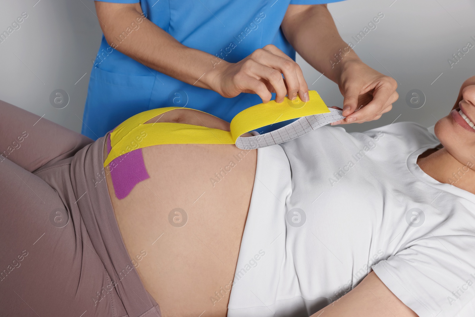 Photo of Pregnant woman visiting physiotherapist. Doctor applying kinesio tape, closeup