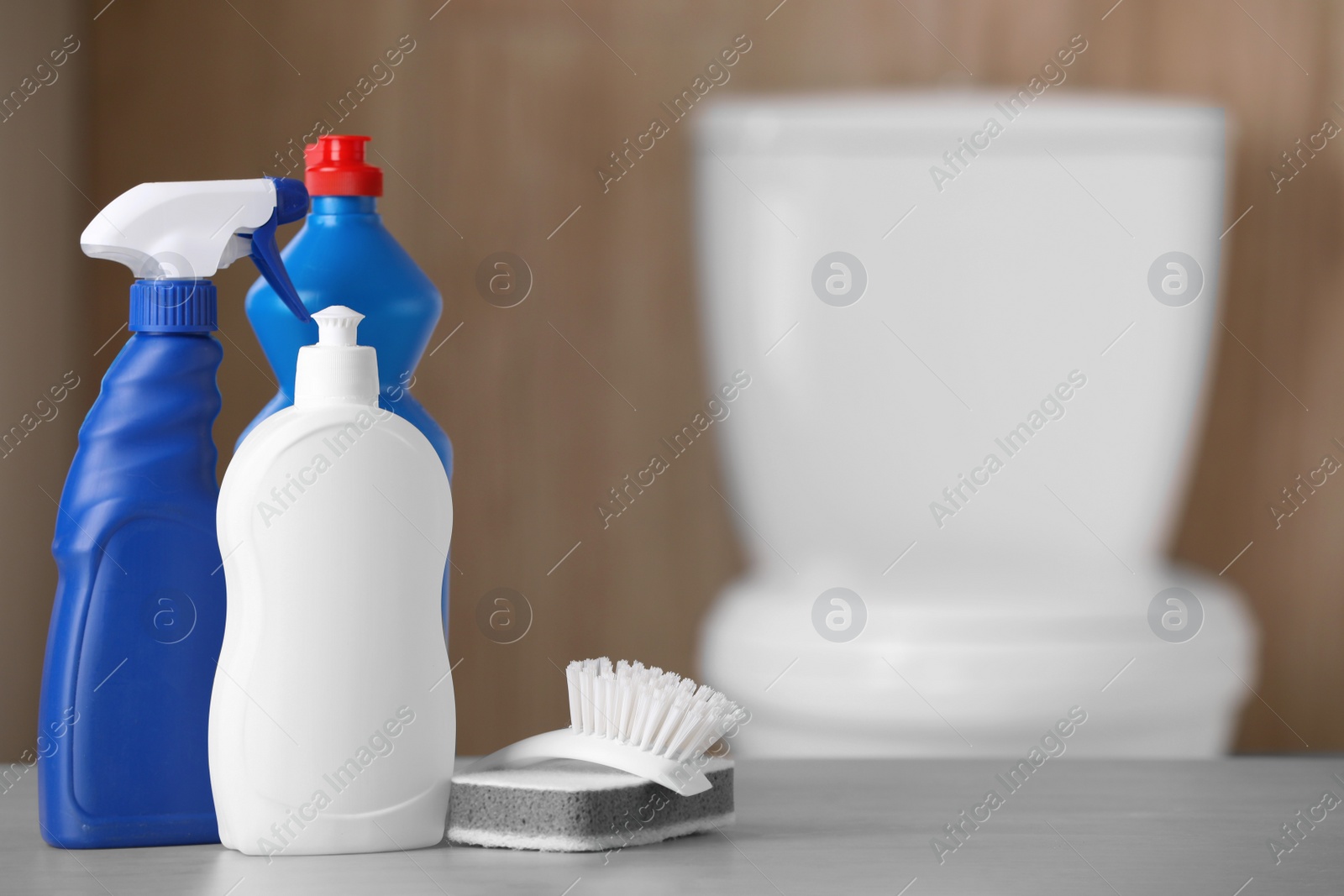 Photo of Bottles, sponge and toilet brush on table indoors, space for text. Cleaning supplies