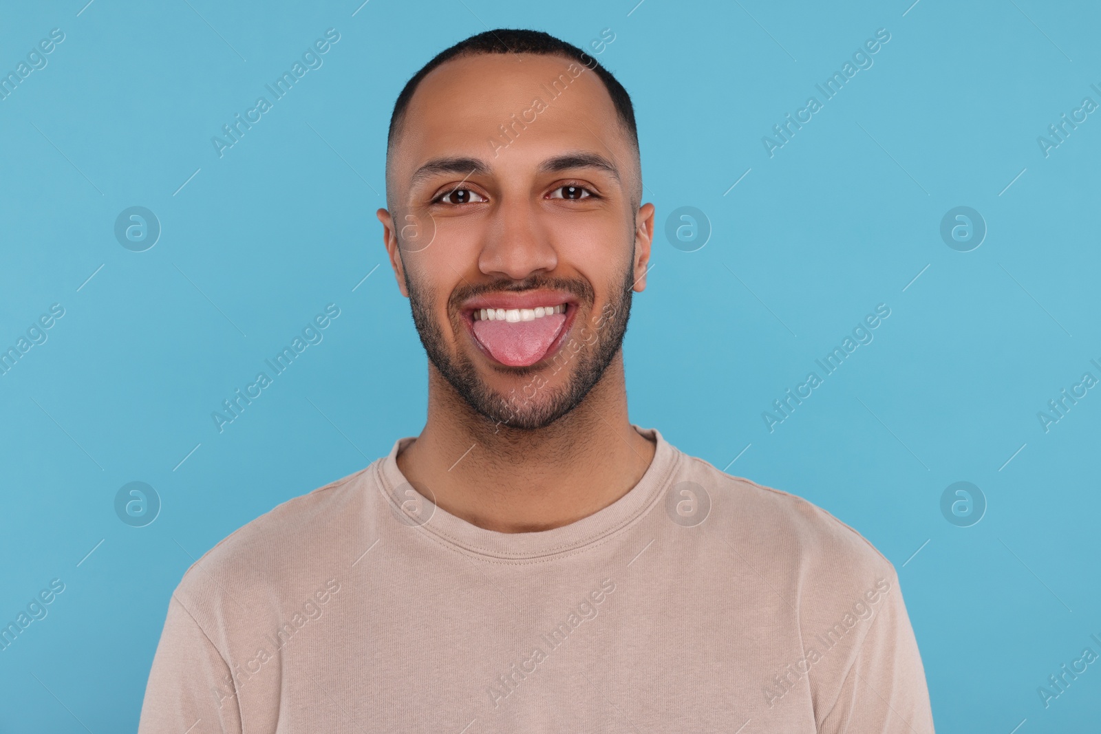 Photo of Happy young man showing his tongue on light blue background