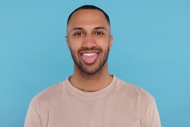 Photo of Happy young man showing his tongue on light blue background
