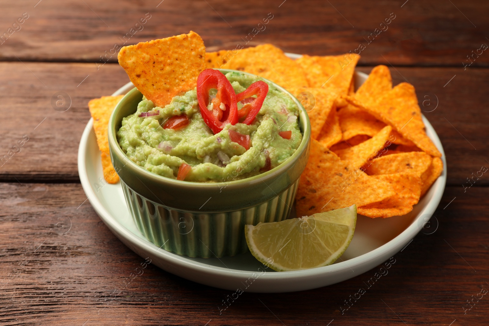 Photo of Bowl of delicious guacamole, nachos chips and lime on wooden table, closeup