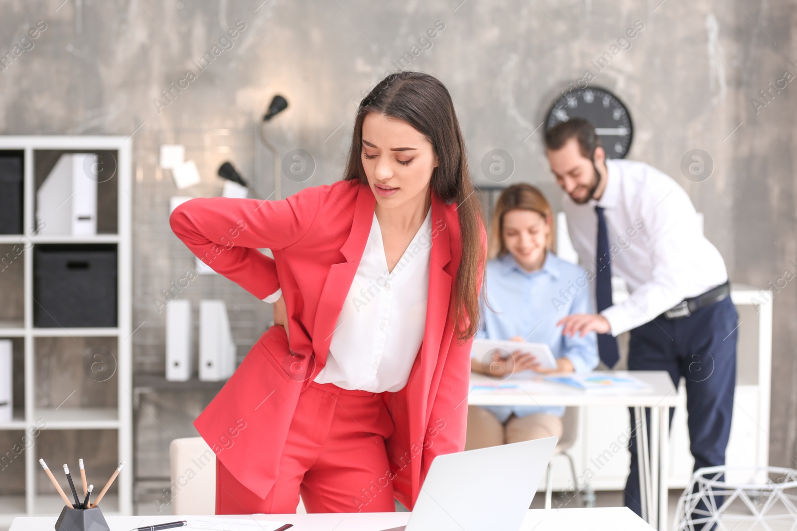 Photo of Young woman suffering from back pain in office