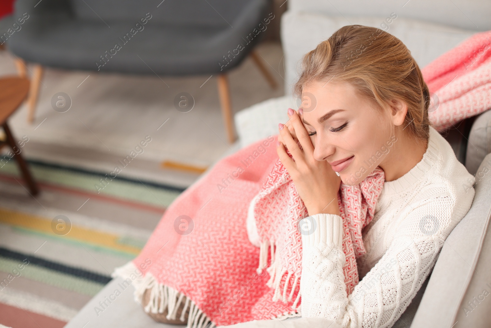 Photo of Beautiful young woman wrapped in plaid sitting on sofa at home. Winter atmosphere