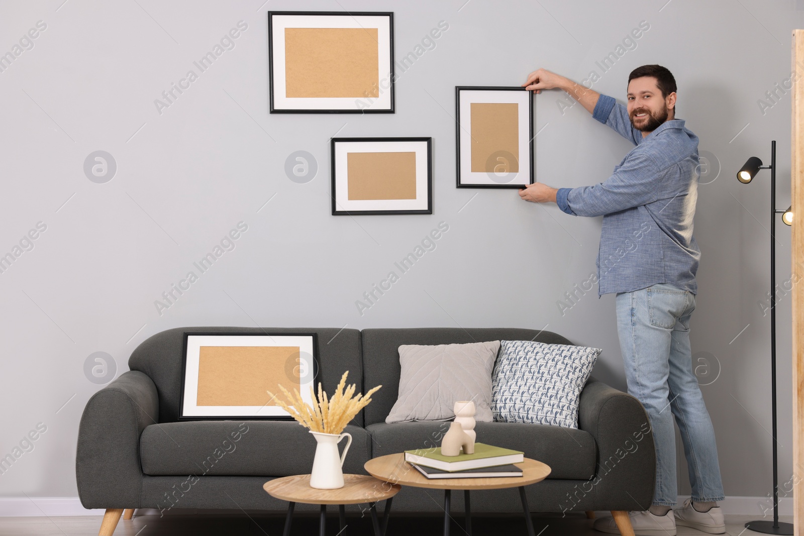 Photo of Man hanging picture frame on gray wall at home