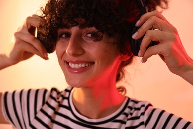 Beautiful young woman listening to music with headphones on color background in neon lights, closeup