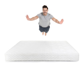 Young man jumping on mattress against white background