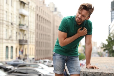 Young man having heart attack on city street. Space for text