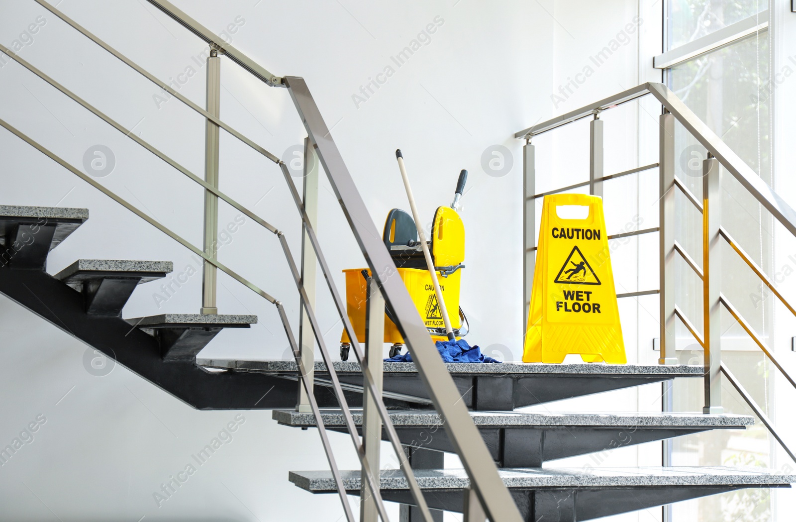 Photo of Safety sign with phrase Caution wet floor and mop bucket on stairs. Cleaning service