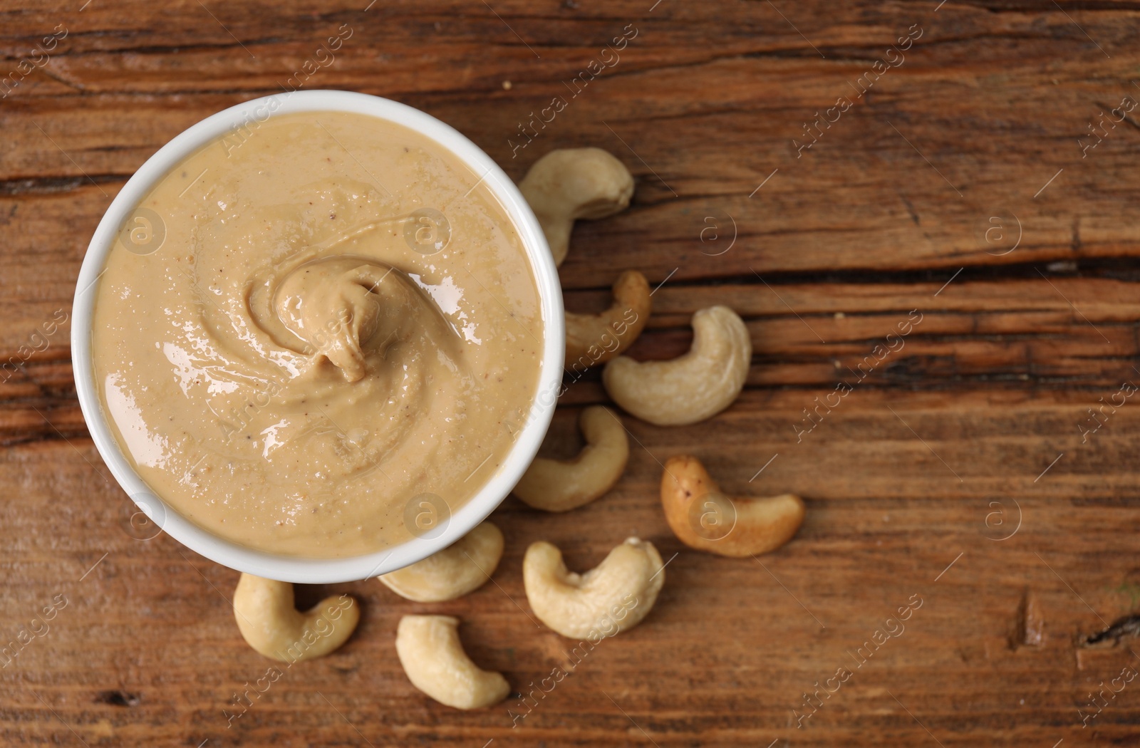 Photo of Delicious nut butter in bowl and cashews on wooden table, top view