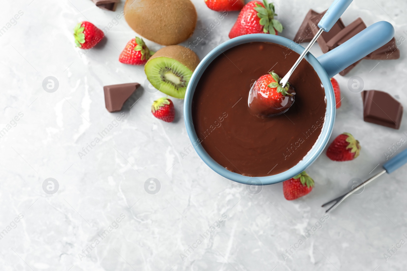 Photo of Dipping strawberry into fondue pot with chocolate on light grey marble table, top view. Space for text