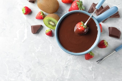 Dipping strawberry into fondue pot with chocolate on light grey marble table, top view. Space for text