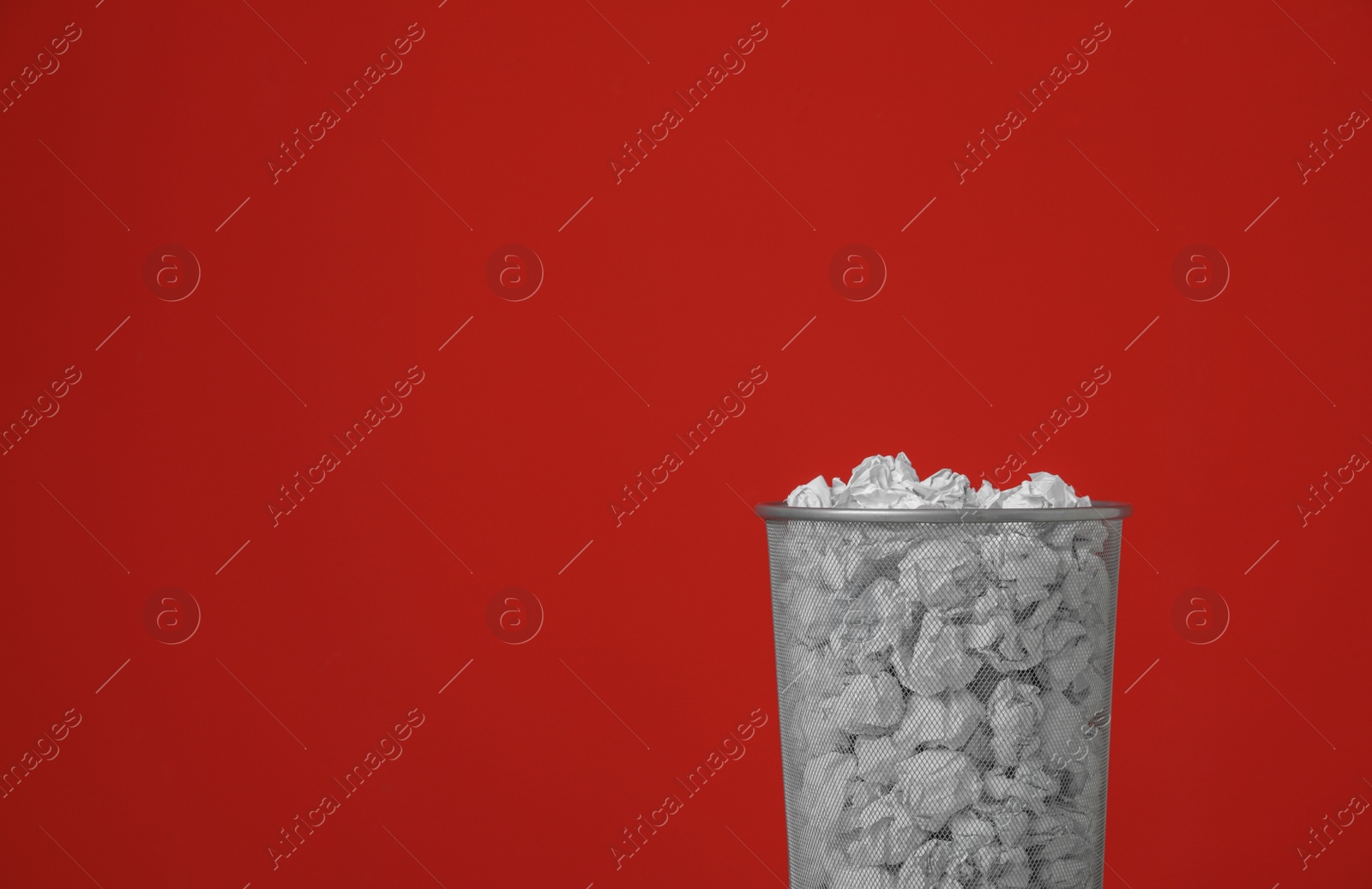 Photo of Metal bin with crumpled paper against color background. Space for text