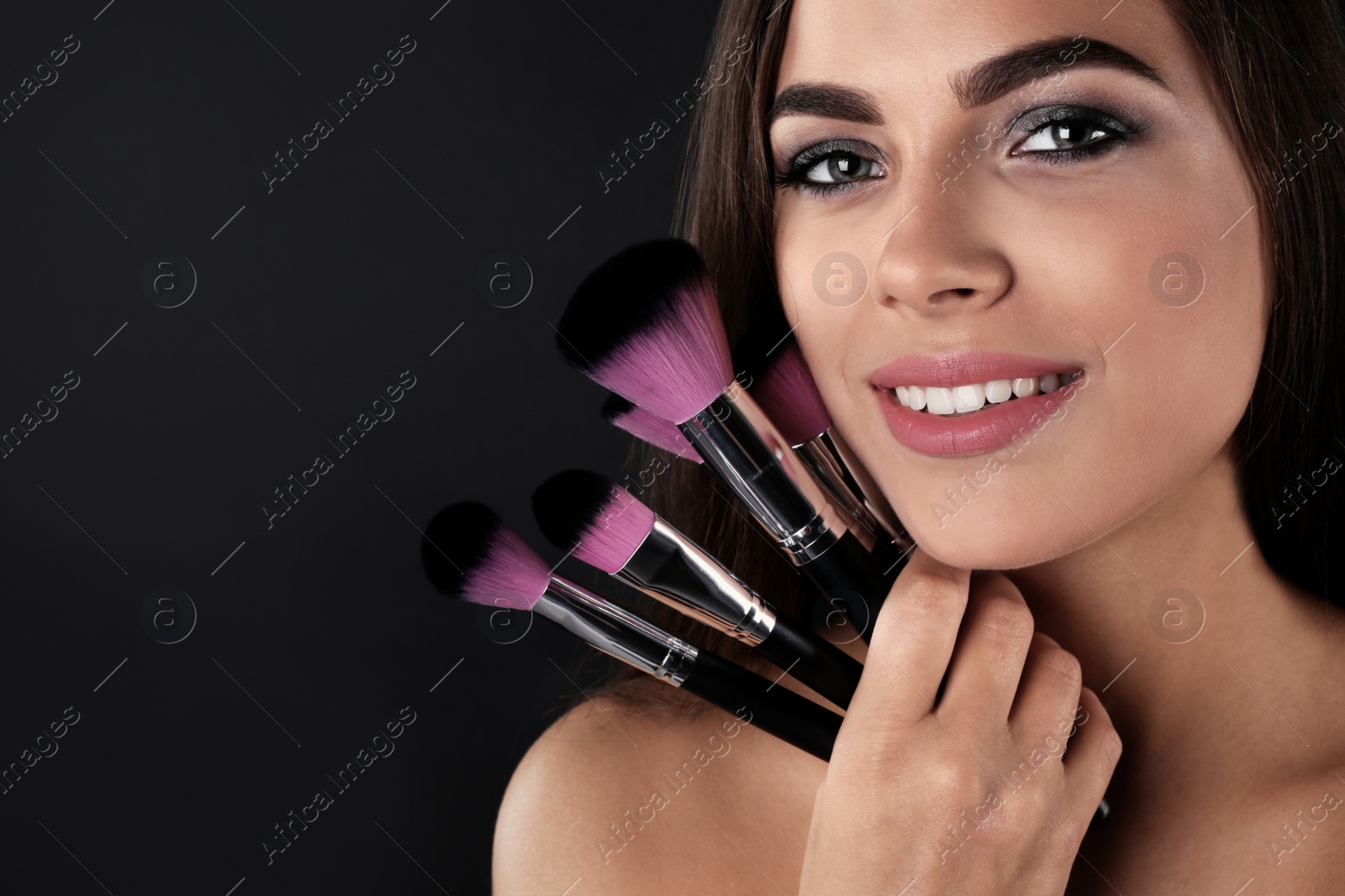 Photo of Portrait of beautiful woman with makeup brushes on dark background. Space for text