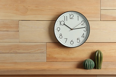 Stylish analog clock hanging on wooden wall. Space for text